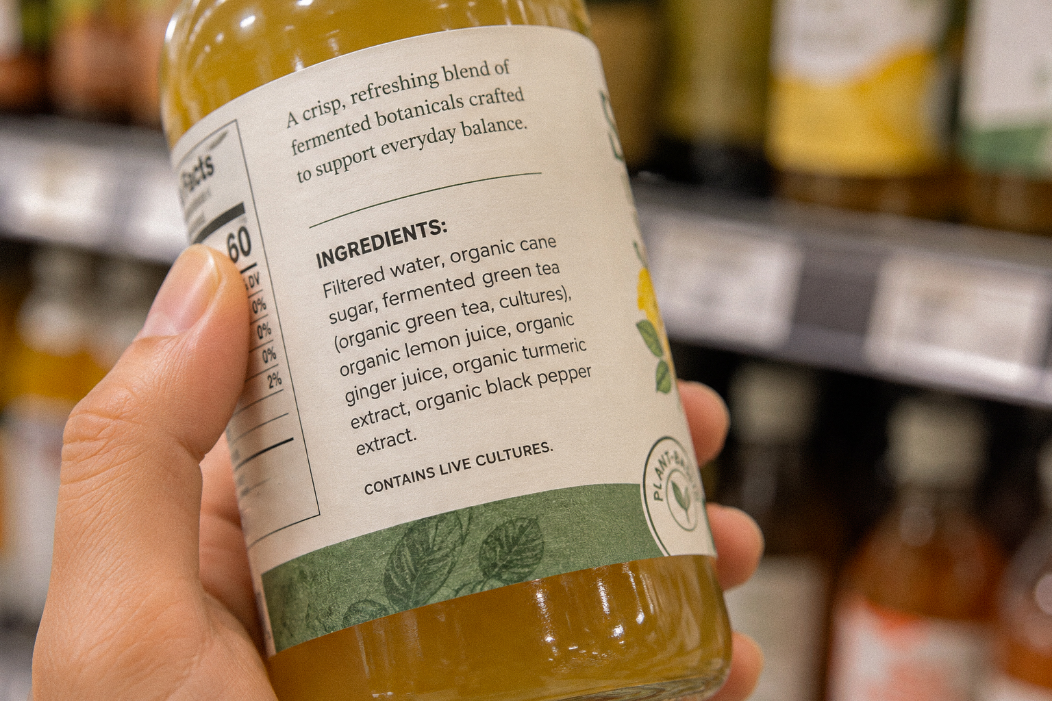 Close-up of a clean-label fermented green tea beverage ingredient list held in front of a store shelf